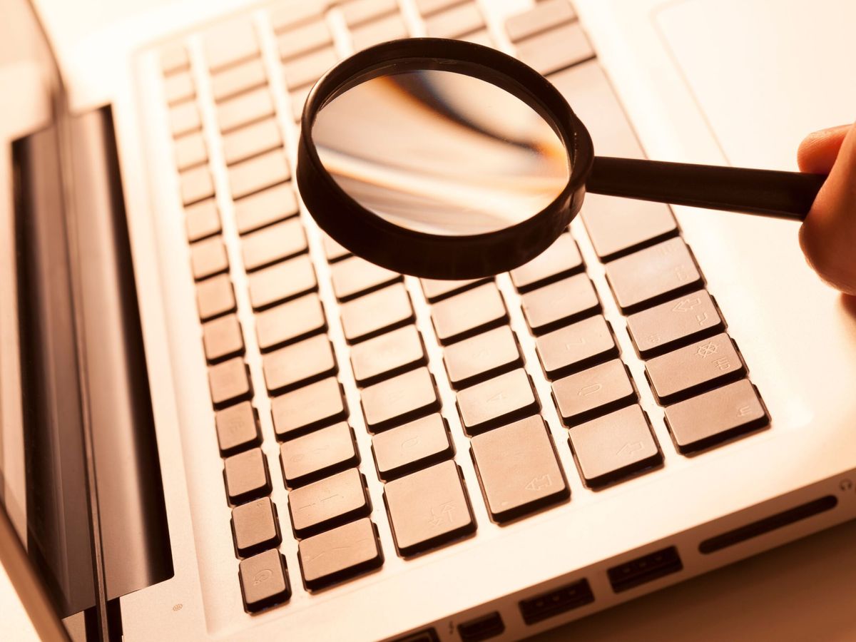 Hand holding a magnifying glass over a laptop keyboard, stock research tools article